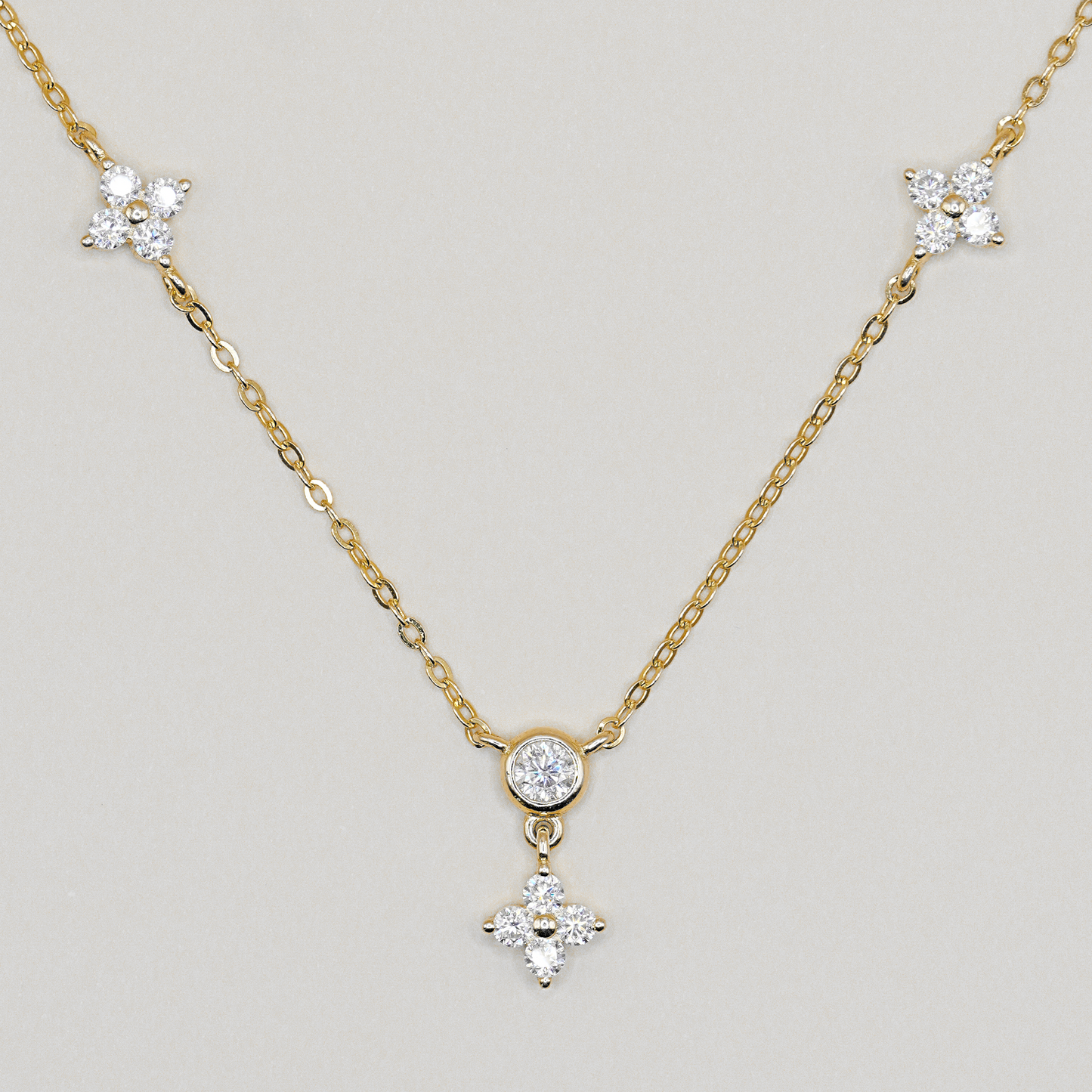A delicate yellow gold chain necklace featuring three star-shaped clusters of clear stones, with a central round clear stone and a dangling four-pointed star pendant, shown on a neutral light gray background.