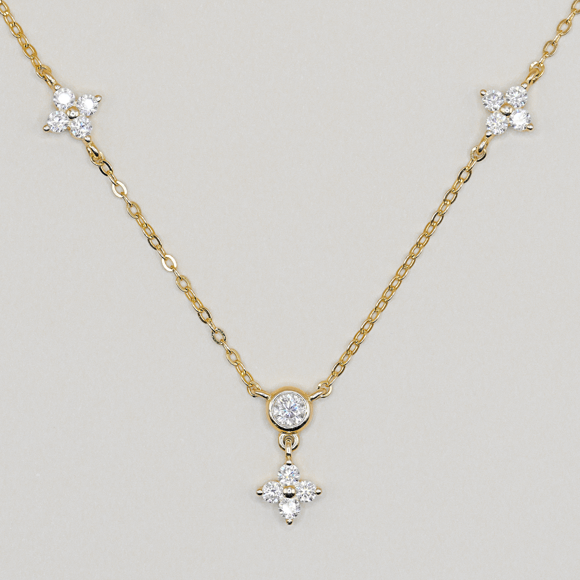 A delicate yellow gold chain necklace featuring three star-shaped clusters of clear stones, with a central round clear stone and a dangling four-pointed star pendant, shown on a neutral light gray background.