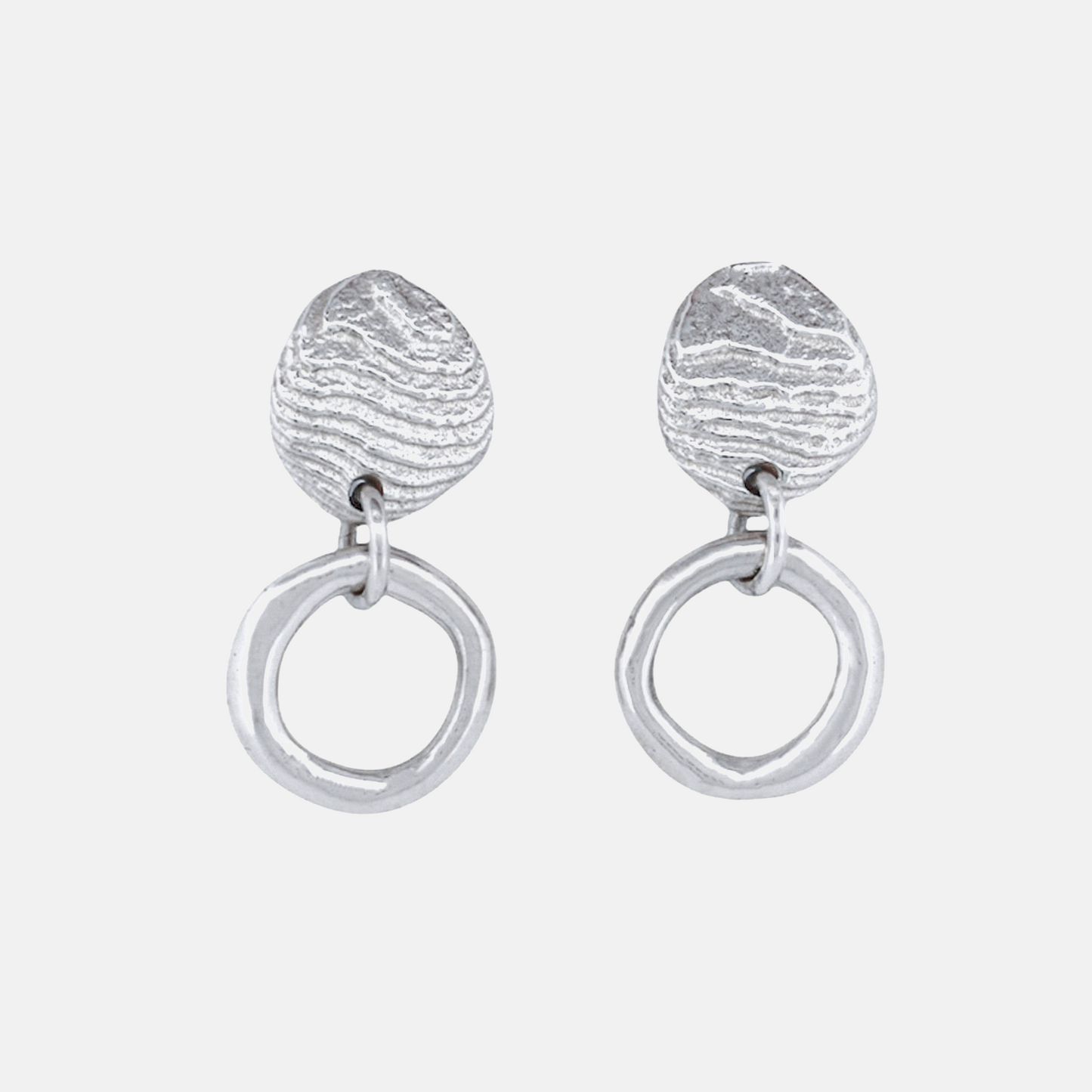 A pair of silver dangle earrings featuring a textured, organic teardrop-shaped top piece connected to a large, polished circular drop, shown on a light gray background.