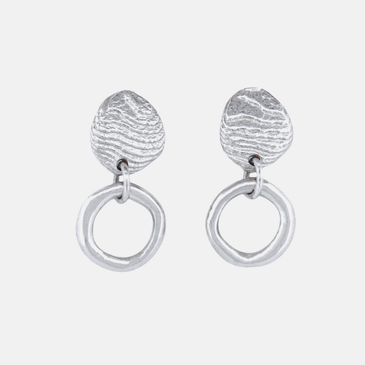 A pair of silver dangle earrings featuring a textured, organic teardrop-shaped top piece connected to a large, polished circular drop, shown on a light gray background.