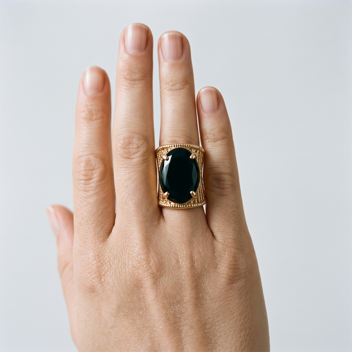 A gold signet ring with a large oval black onyx center stone, worn on a person's ring finger against a light gray background.