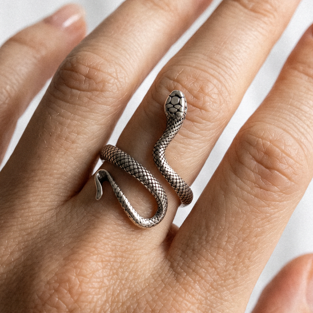 A silver snake wrap ring worn on a person's finger, shown in a close-up lifestyle shot against a soft white background.
