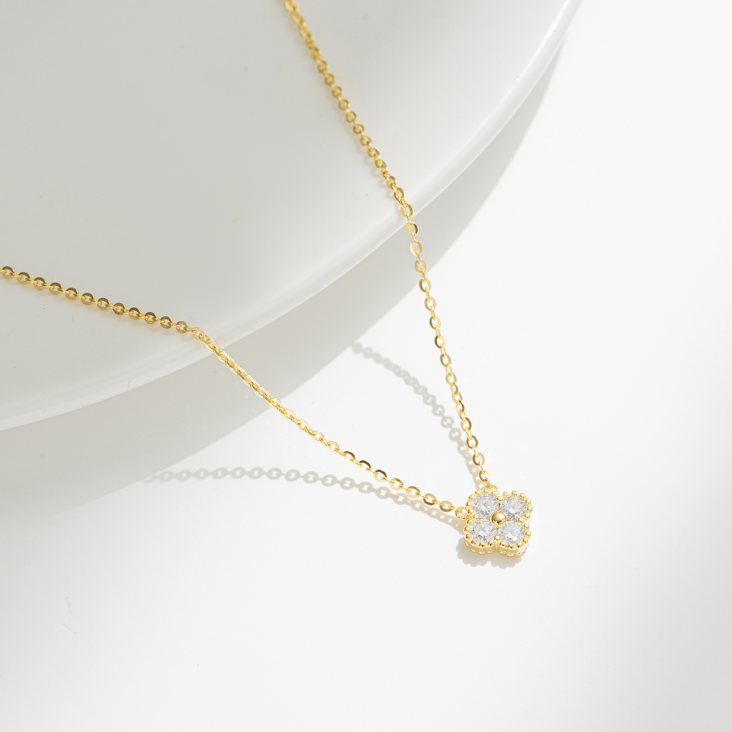 A delicate gold chain necklace with a small flower-shaped pendant set with clear stones, displayed on a clean white surface.