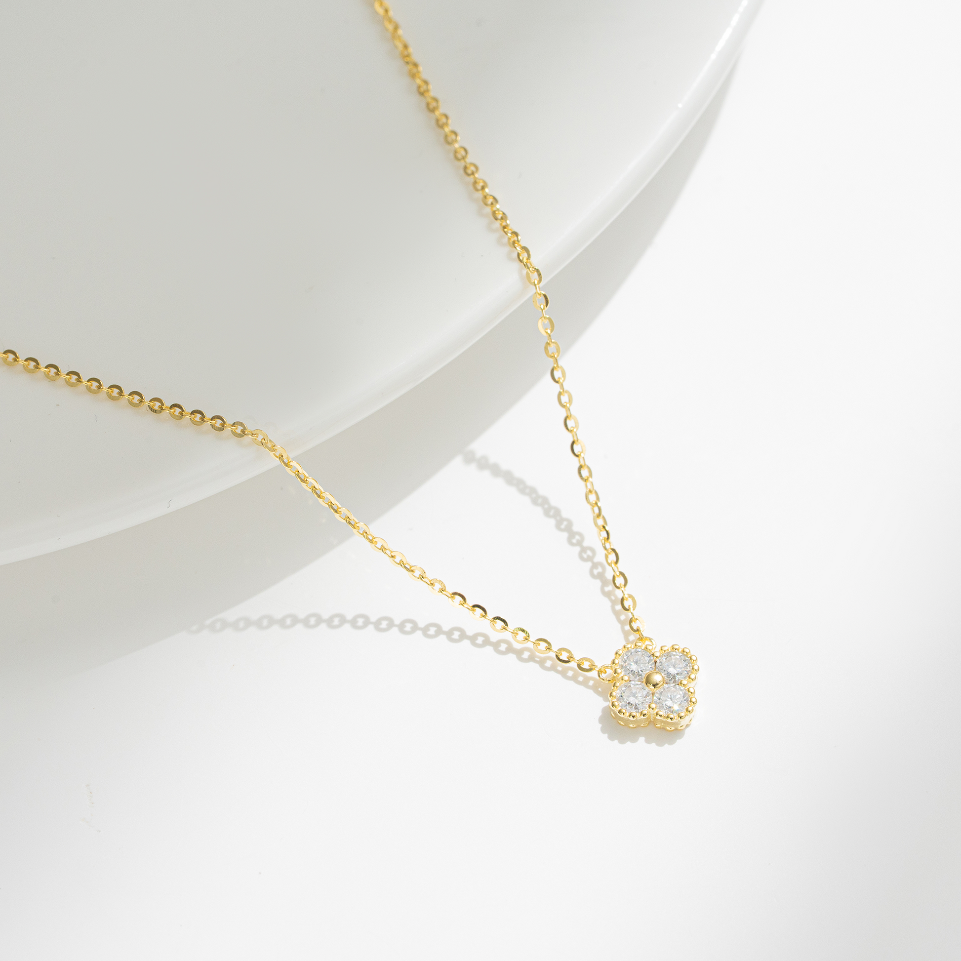 A delicate gold chain necklace with a small flower-shaped pendant set with clear stones, displayed on a clean white surface.