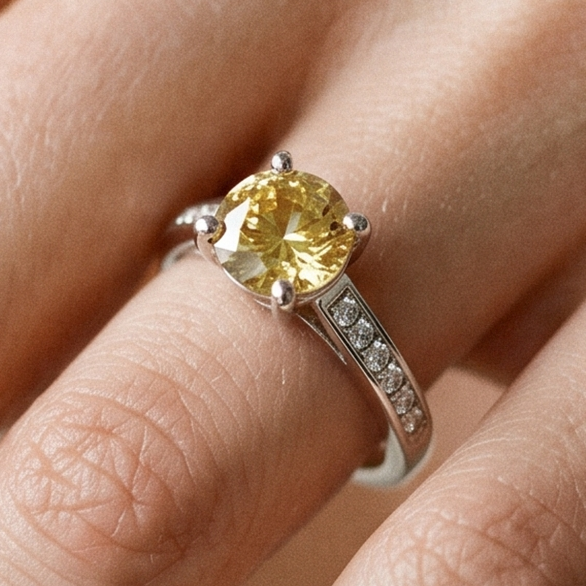 A close-up of a yellow oval-cut gemstone ring with a silver band, worn on a finger.