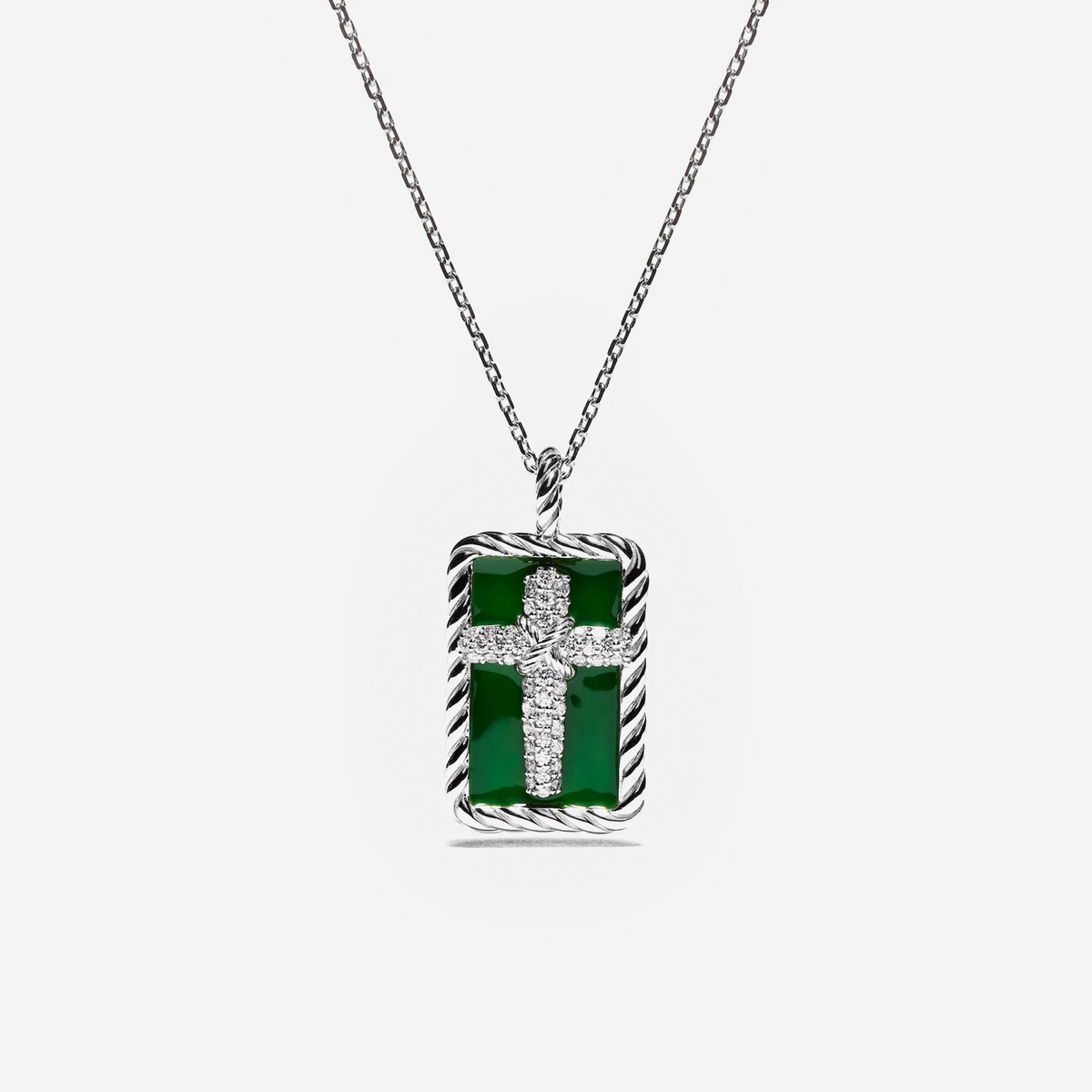 A silver-toned rectangular pendant necklace featuring a green enamel background with a silver cross outlined in small clear stones, suspended from a silver chain on a light gray background.