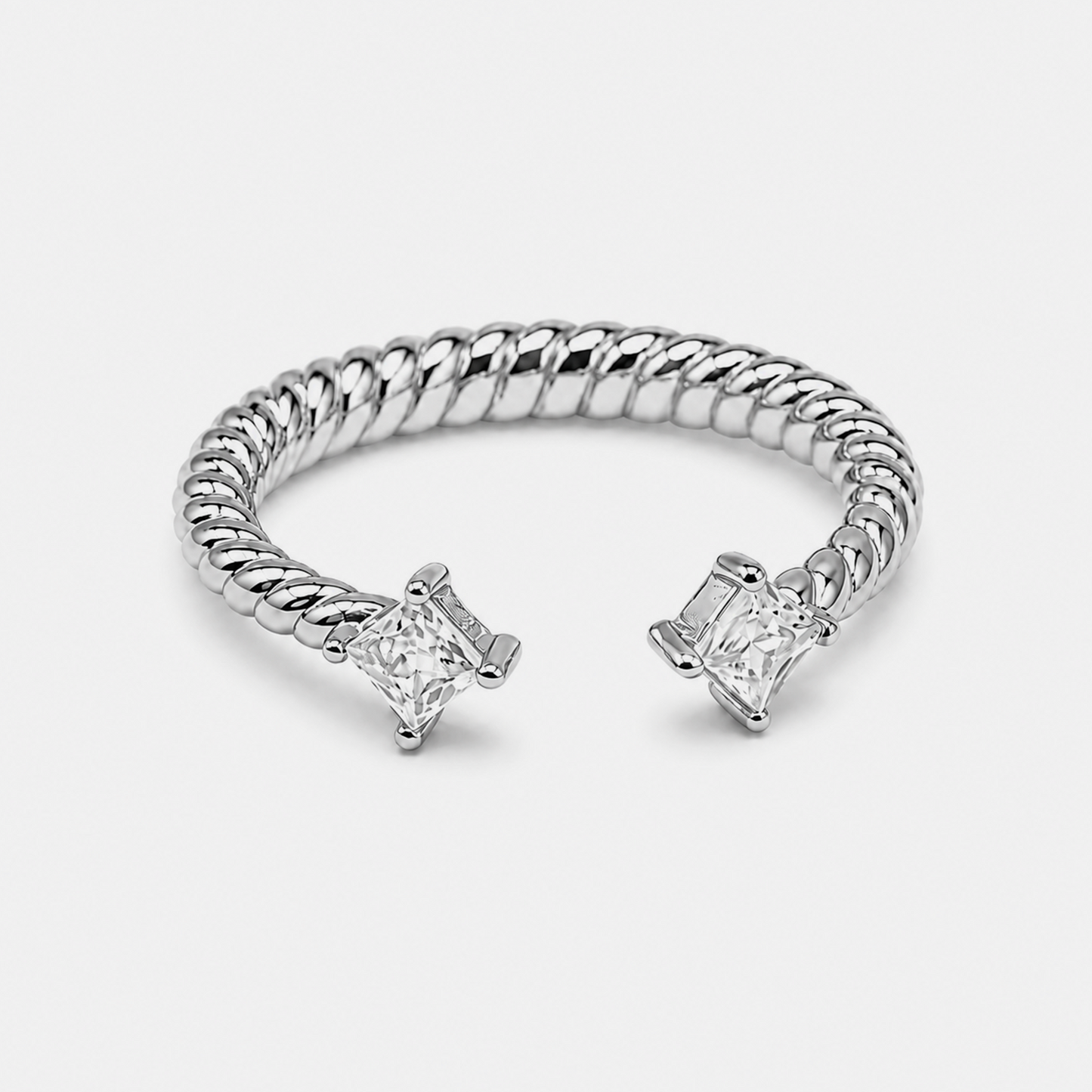 A silver-toned twisted rope cuff ring with two princess-cut clear gemstones, photographed on a clean light gray background.