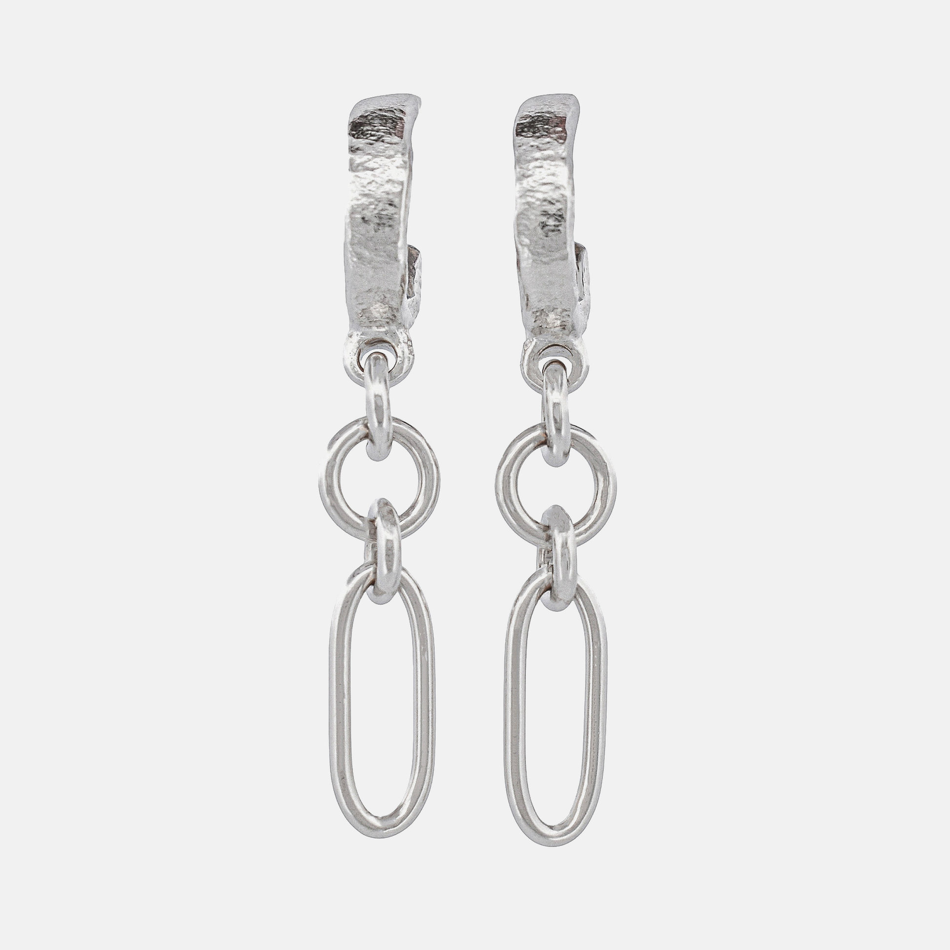 A pair of silver huggie hoop earrings with textured tops and dangling oval links, shown on a light gray background.