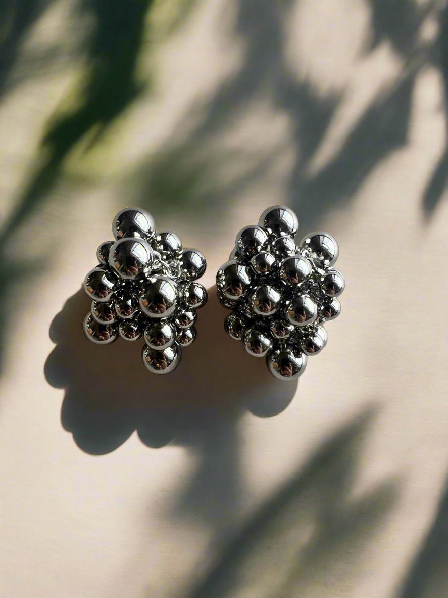 Silver floral earrings on a beige surface with leaf shadows