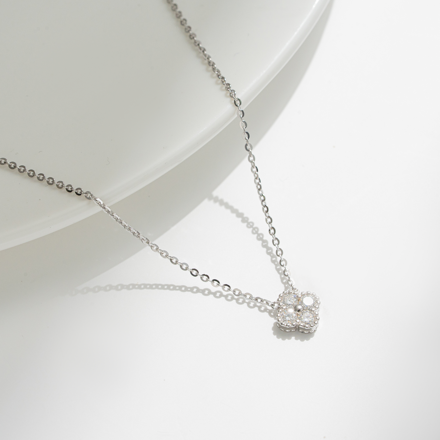 A delicate silver chain necklace with a small, clear-studded flower-shaped pendant, displayed on a clean white surface with a soft shadow.