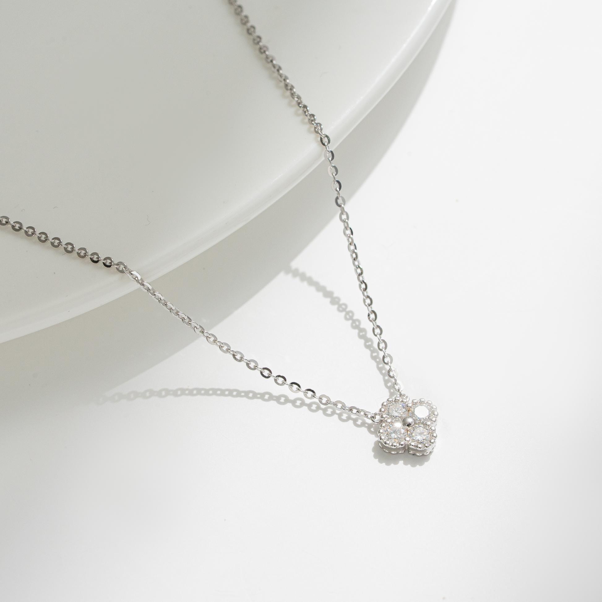 A delicate silver chain necklace with a small, clear-studded flower-shaped pendant, displayed on a clean white surface with a soft shadow.