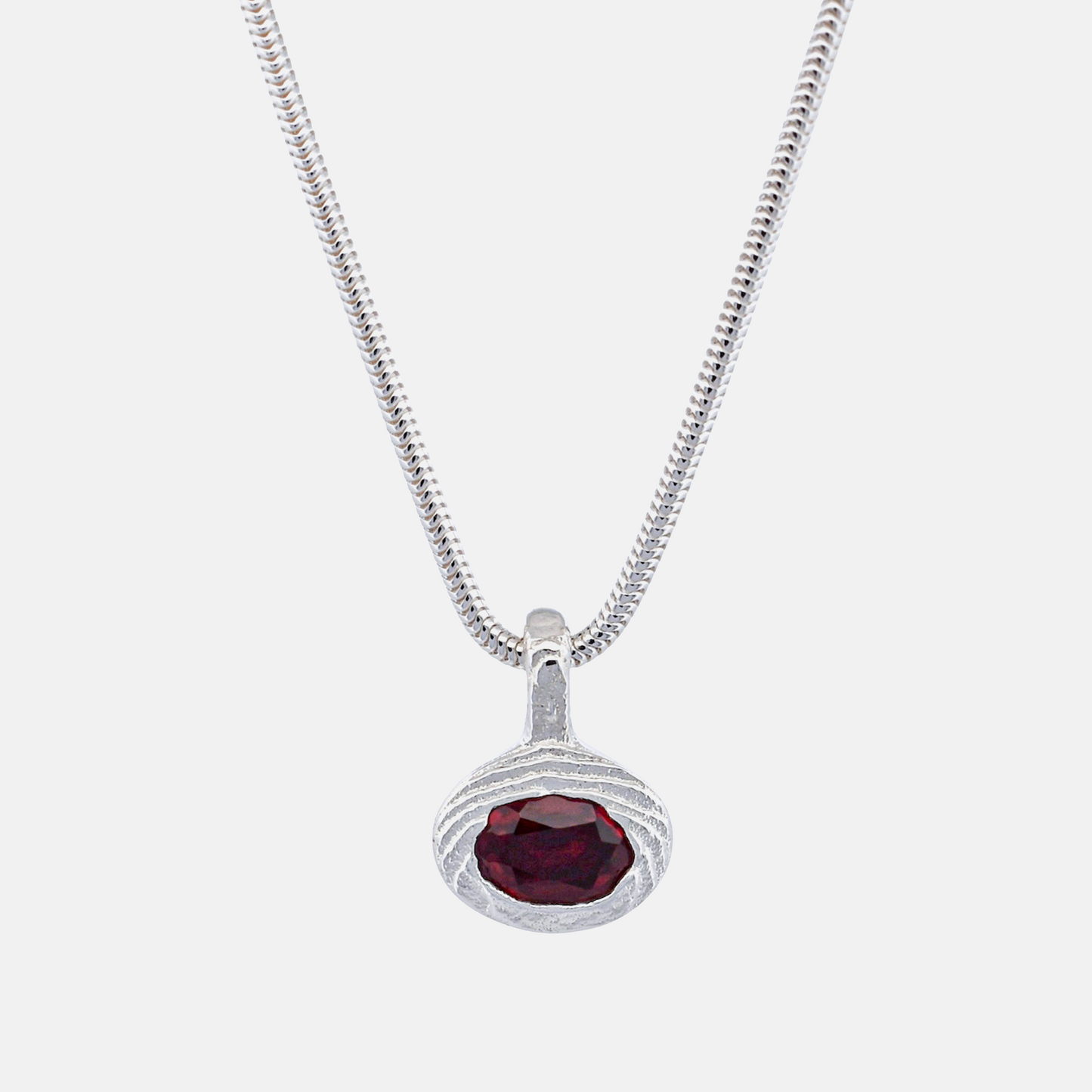 A silver snake chain necklace with a textured oval pendant featuring a faceted dark red gemstone, shown against a plain white background.