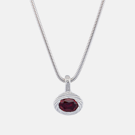 A silver snake chain necklace with a textured oval pendant featuring a faceted dark red gemstone, shown against a plain white background.