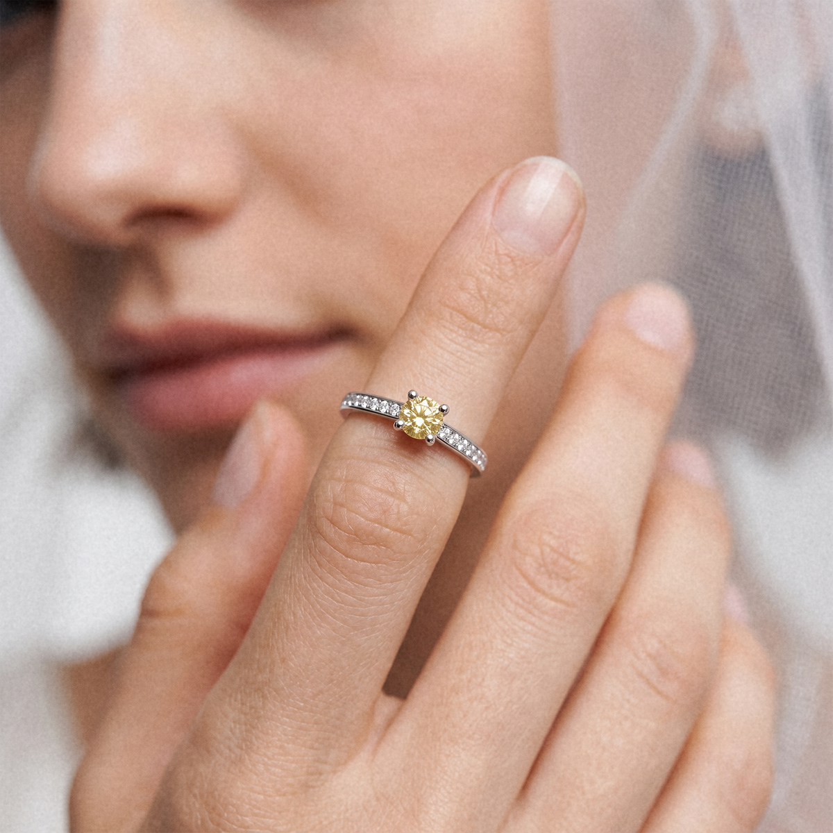 A close-up lifestyle shot of a woman wearing a yellow diamond center stone ring with a silver pavé band, held up to show the jewelry.