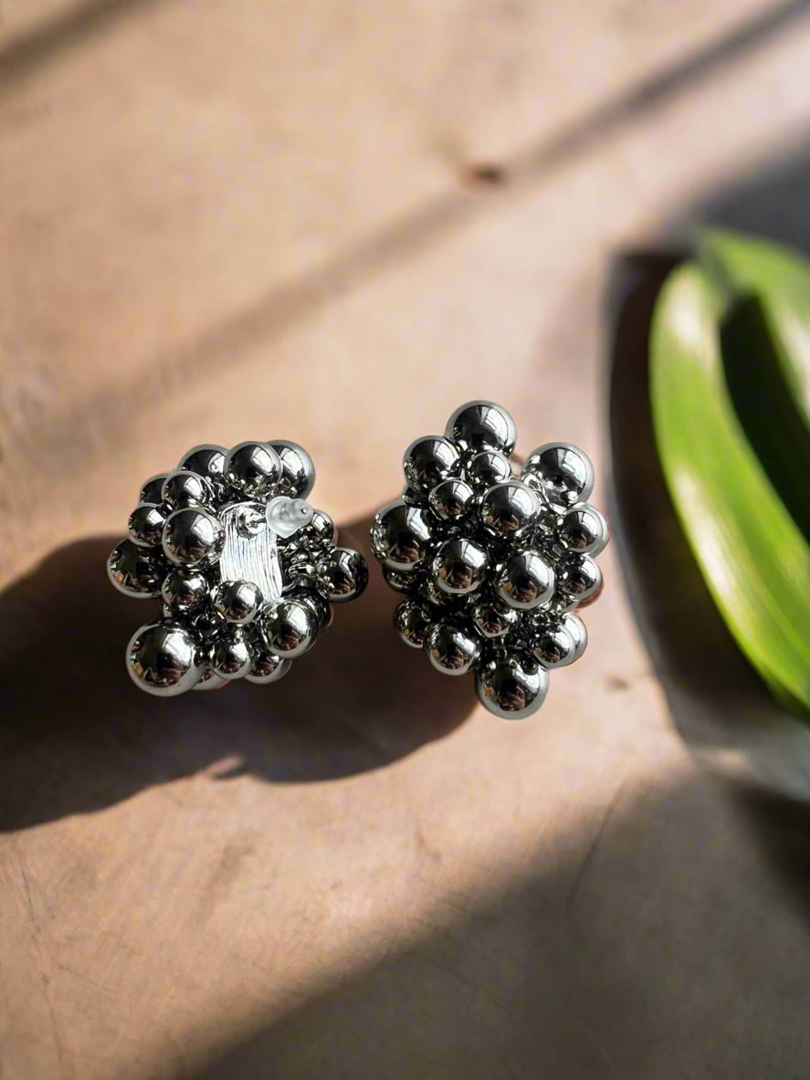 Silver beaded earrings on a wooden surface with a green leaf.