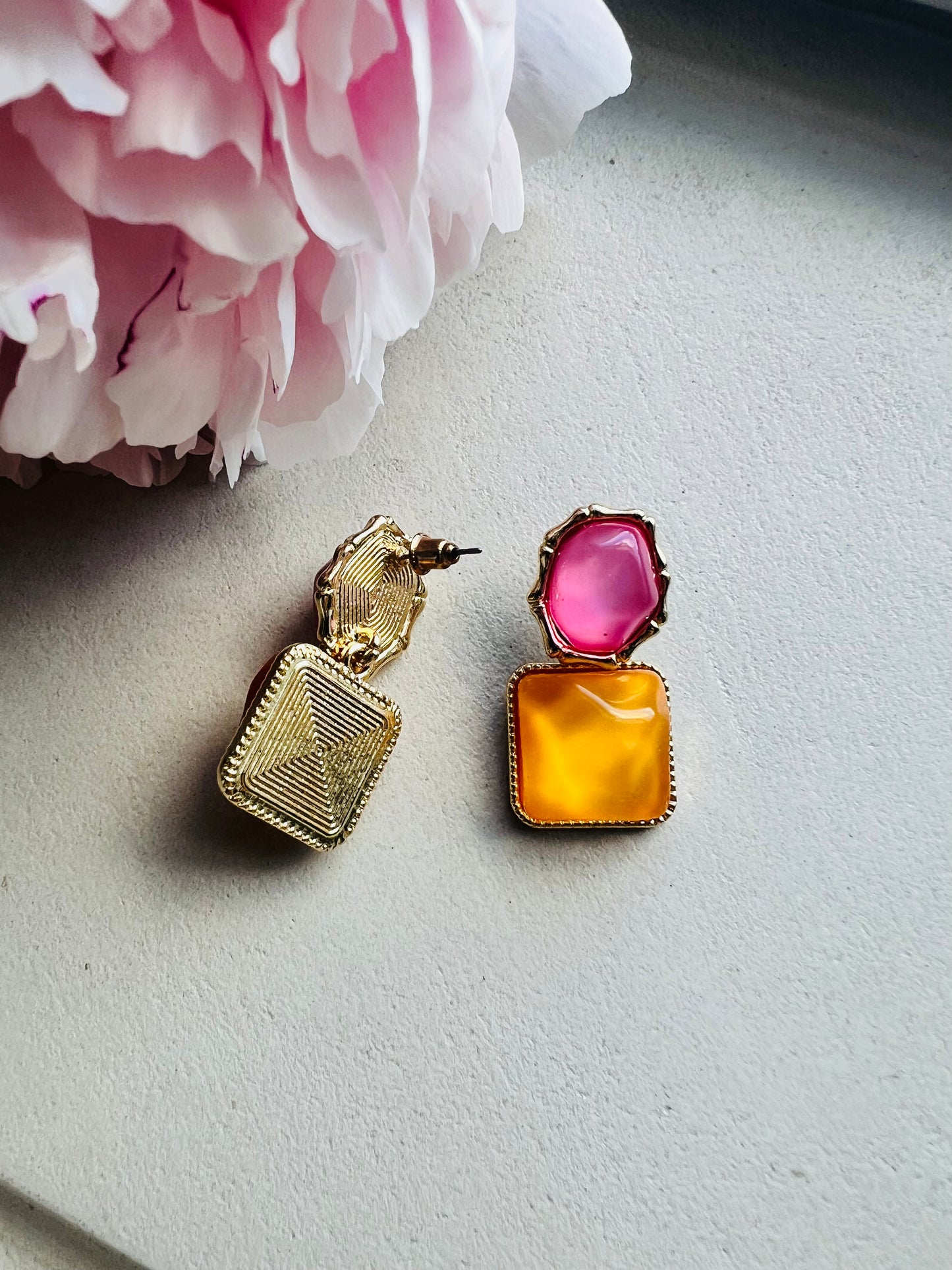 Pair of earrings with pink and orange stones on a light background