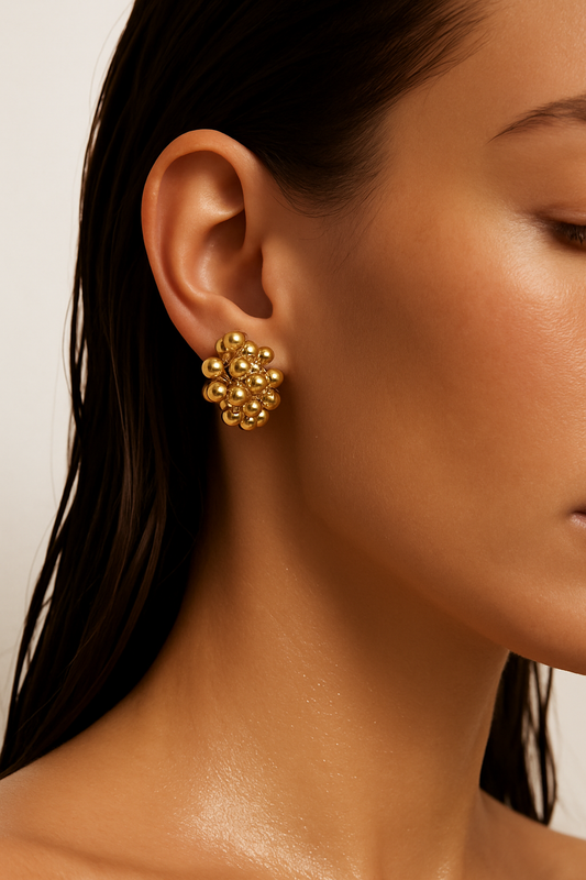 Close-up of a person wearing gold floral earrings with a neutral background