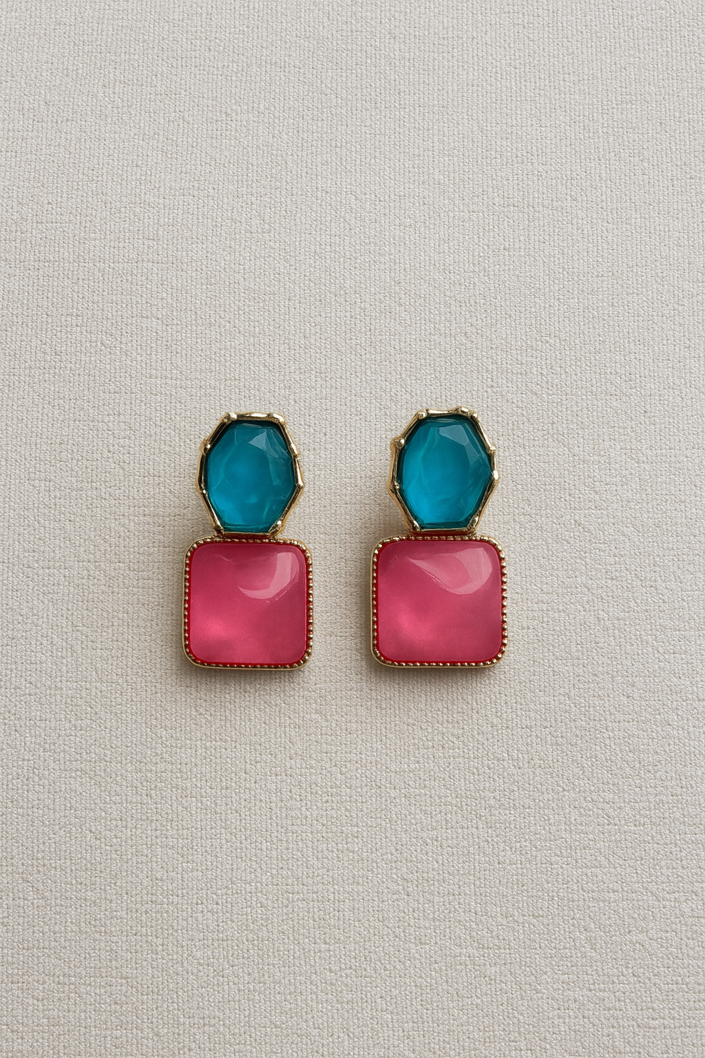 Pair of earrings with pink square and blue teardrop design on a light gray background