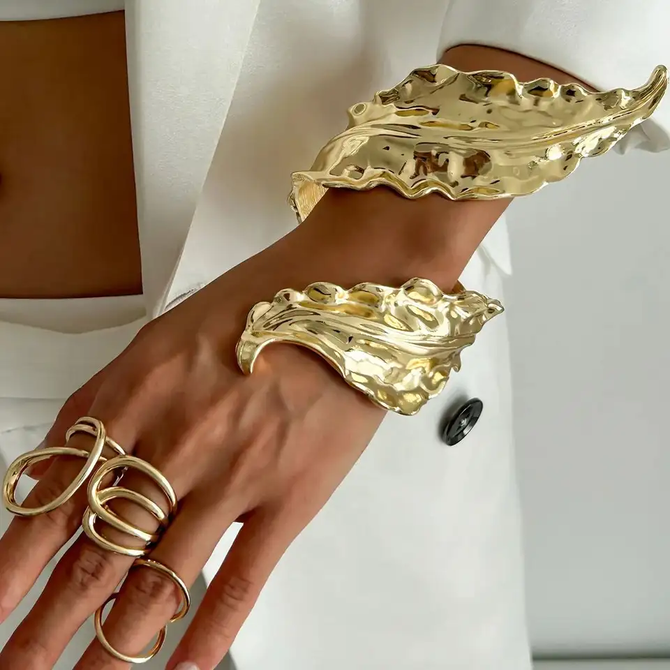 A gold-tone metal cuff bracelet with a leaf pattern.