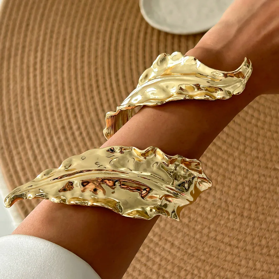 A gold-tone metal cuff bracelet with a leaf pattern.