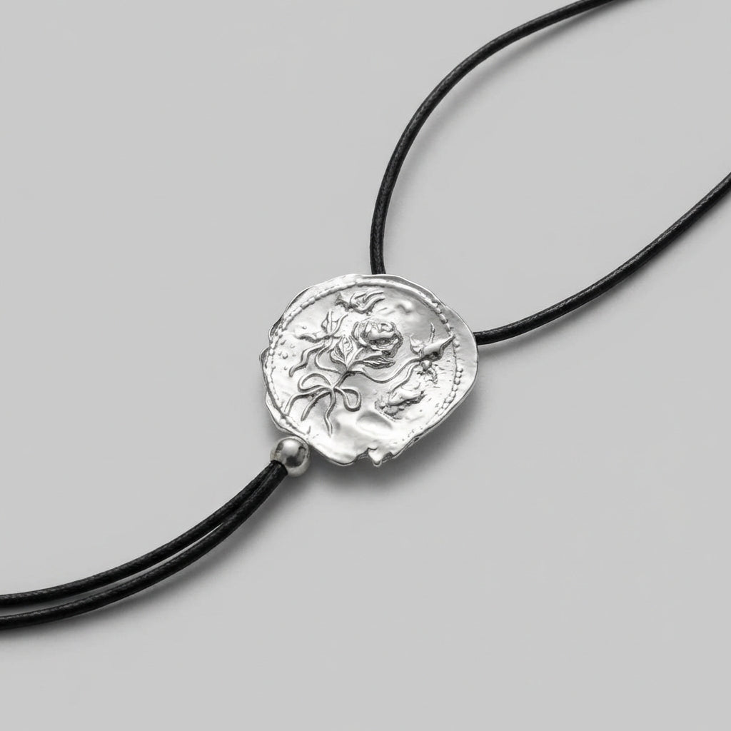 Silver pendant on a black cord against a gray background