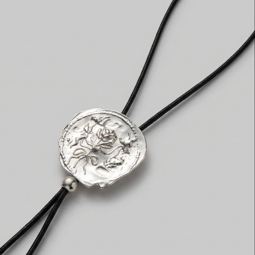 Silver pendant on a black cord against a gray background