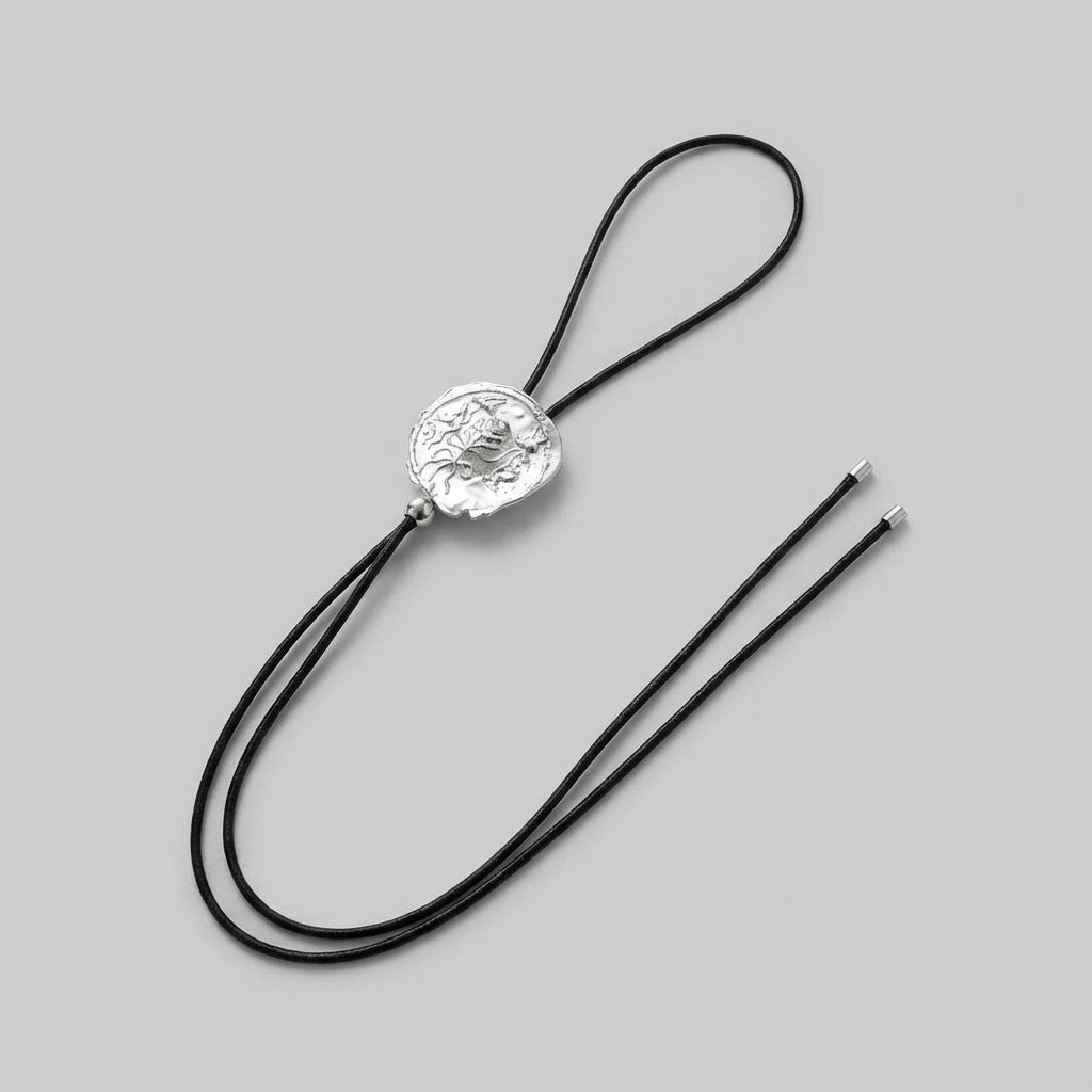 Silver bolo tie with black cord on a gray background