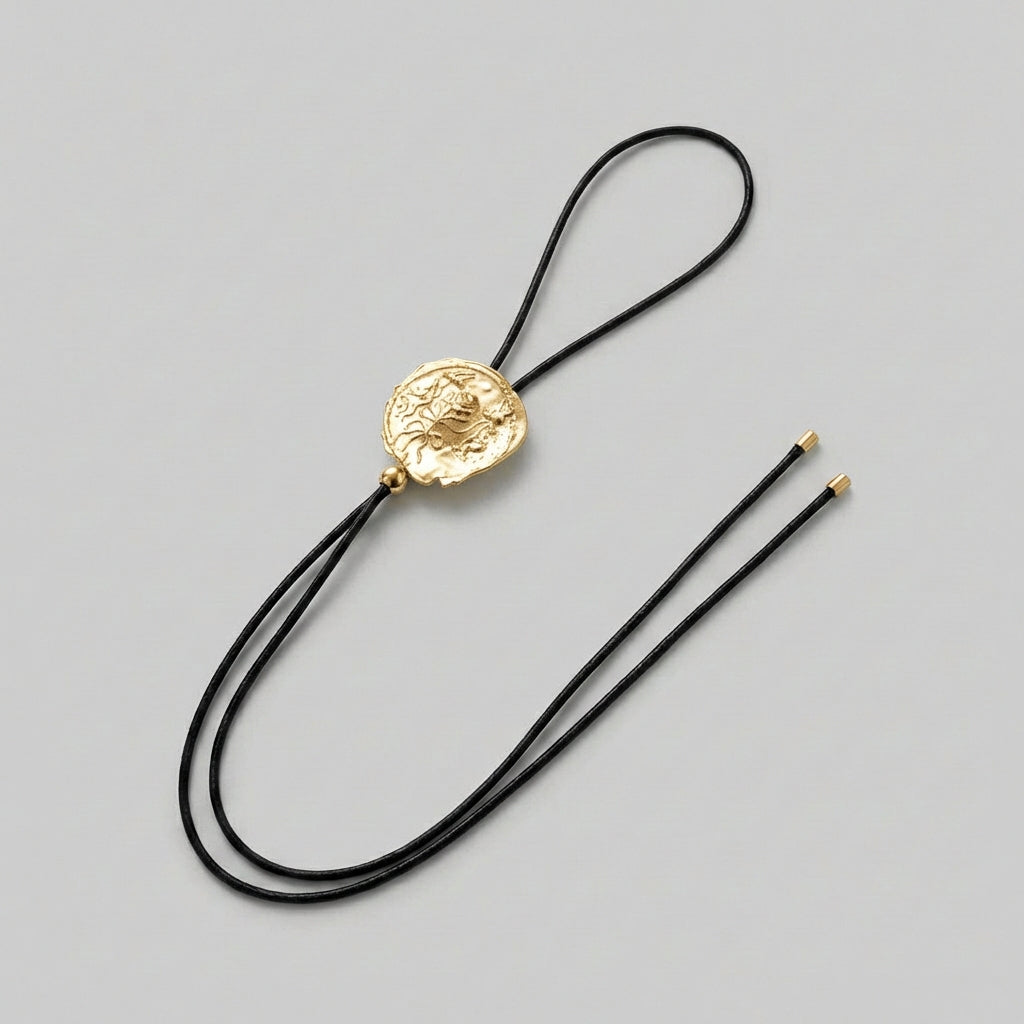 Gold bolo tie with black cord on a gray background