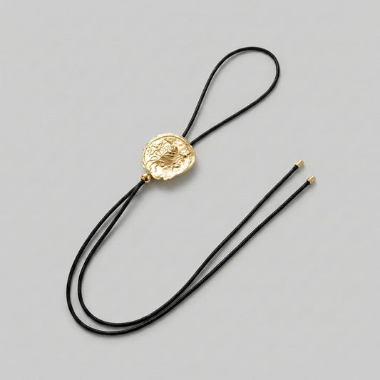 Gold bolo tie with black cord on a gray background