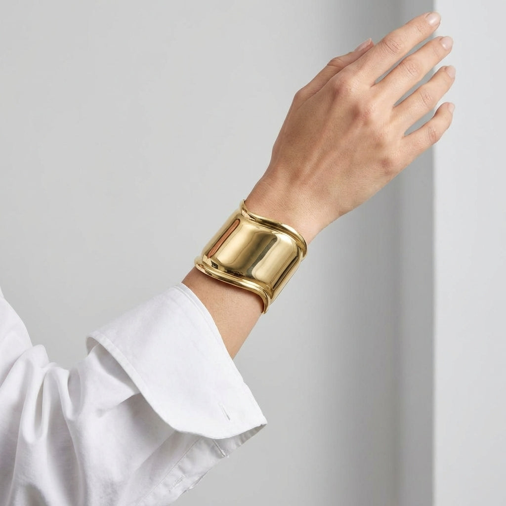 Gold bracelet on a wrist with a white shirt against a light gray background