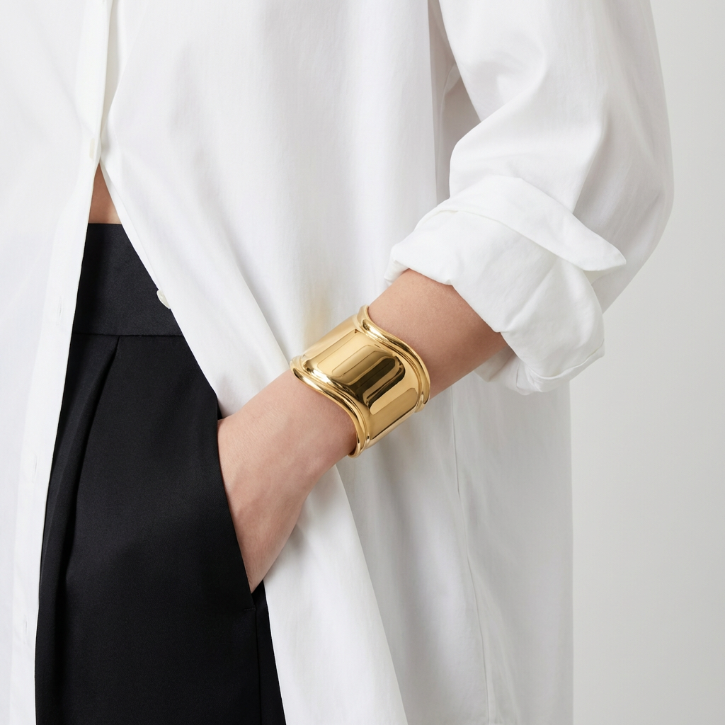 Gold bracelet worn by a person wearing a white shirt against a neutral background