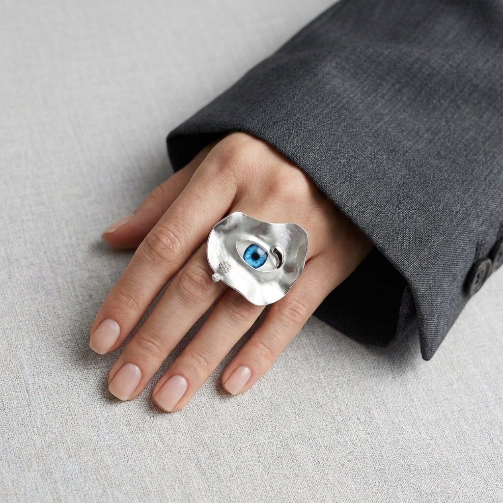 Silver ring with a blue gemstone on a hand against a gray background