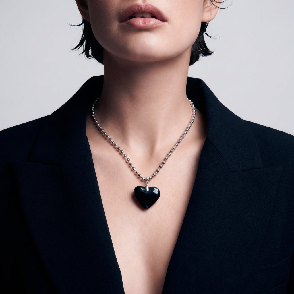 Person wearing a black heart pendant necklace against a neutral background