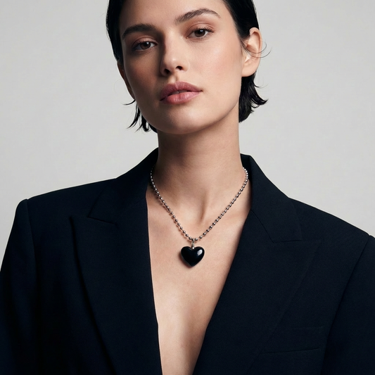 Woman wearing a black heart pendant necklace against a plain background