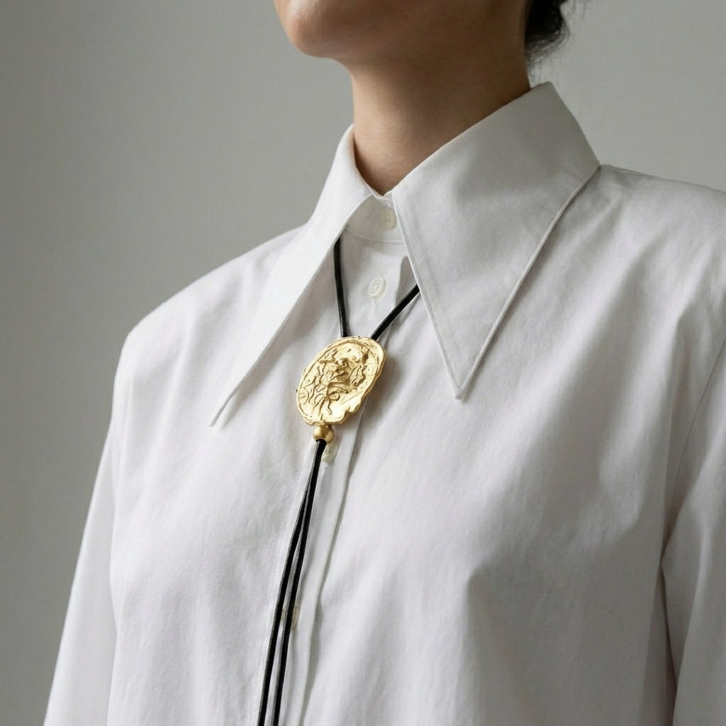 Gold bolo tie on a white shirt against a neutral background