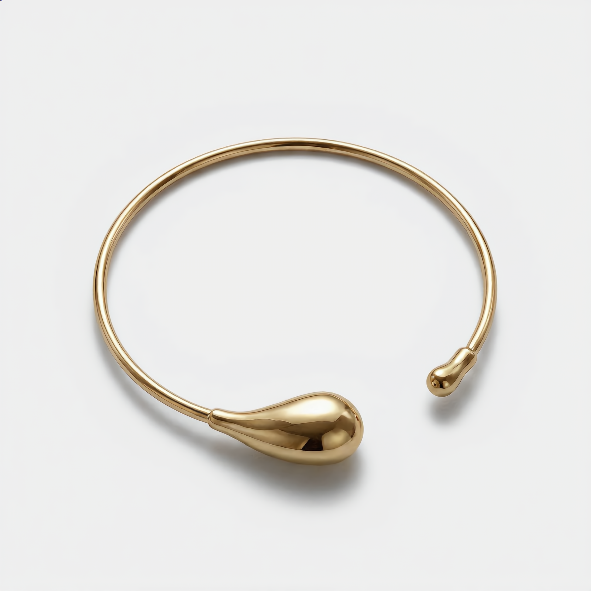 Gold bangle with teardrop design on a light gray background