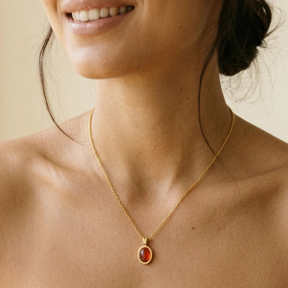 Close-up of a person wearing a gold necklace with a red stone pendant on a neutral background