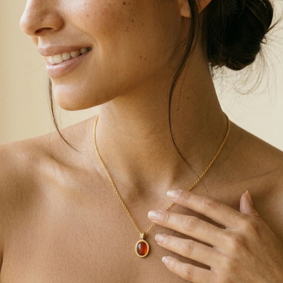 Woman wearing a gold necklace with a red pendant against a neutral background