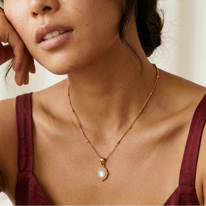 Woman wearing a gold necklace with a pendant against a neutral background